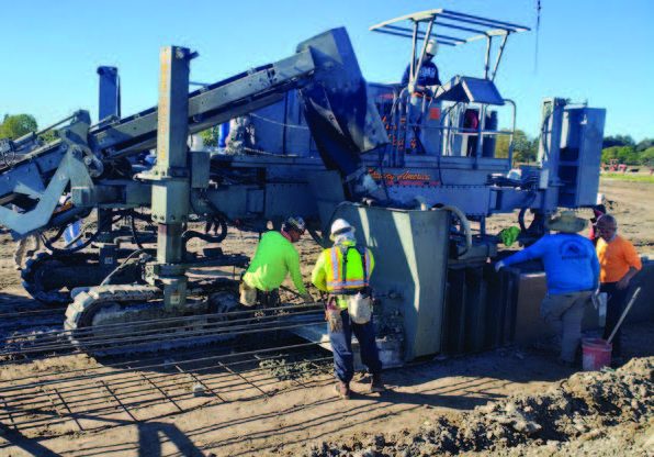 Slipform machine forming rebar-reinforced concrete with crew working at a job site