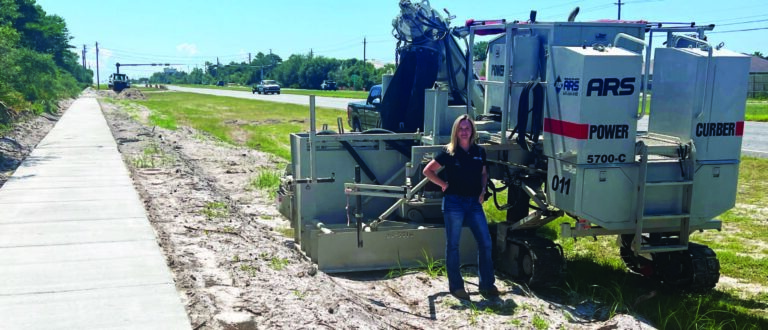 Woman standing beside a Power Curber 5700-C next to a finished concrete sidewalk along a highway