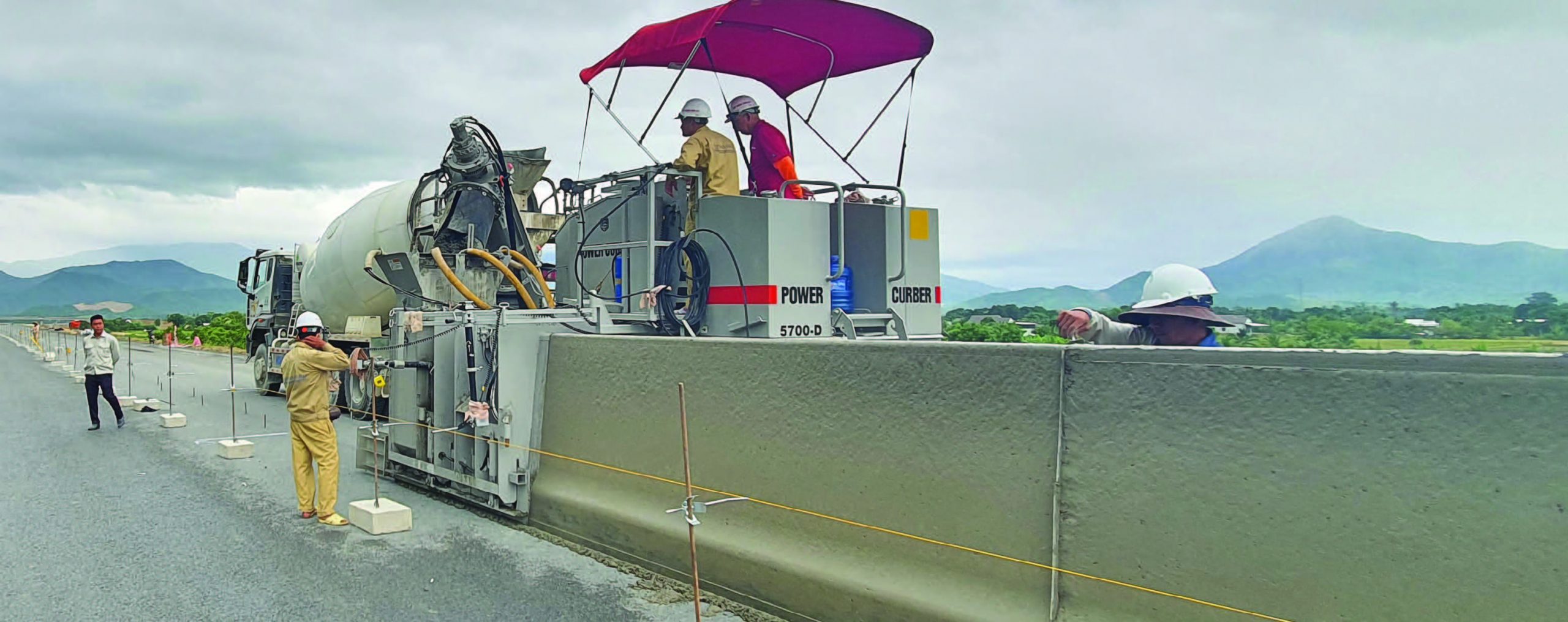 Power Curber 5700-D pouring a concrete barrier on a highway in Vietnam with mountains behind