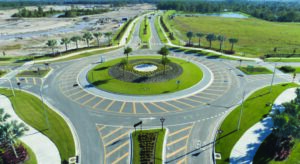 Aerial view of a landscaped roundabout with palm trees, crosswalks, and newly placed concrete curbing.