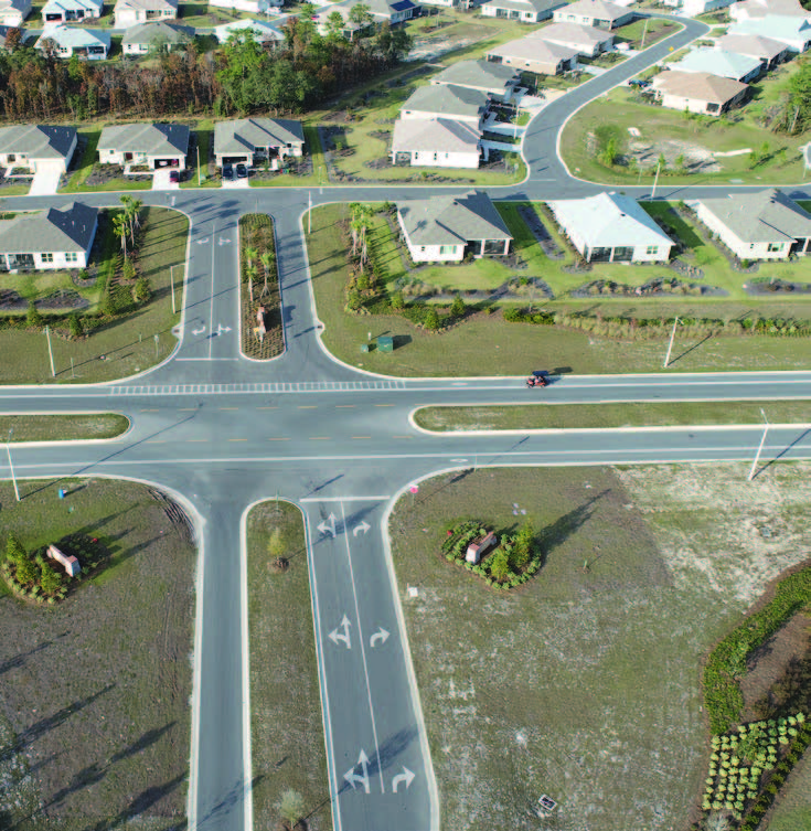 Aerial view of a residential street intersection with concrete curbing, turn-lane markings, and single-family homes.