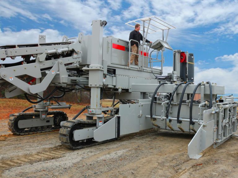 Power Curber machine paving concrete on a dirt site, with a worker standing on the platform.