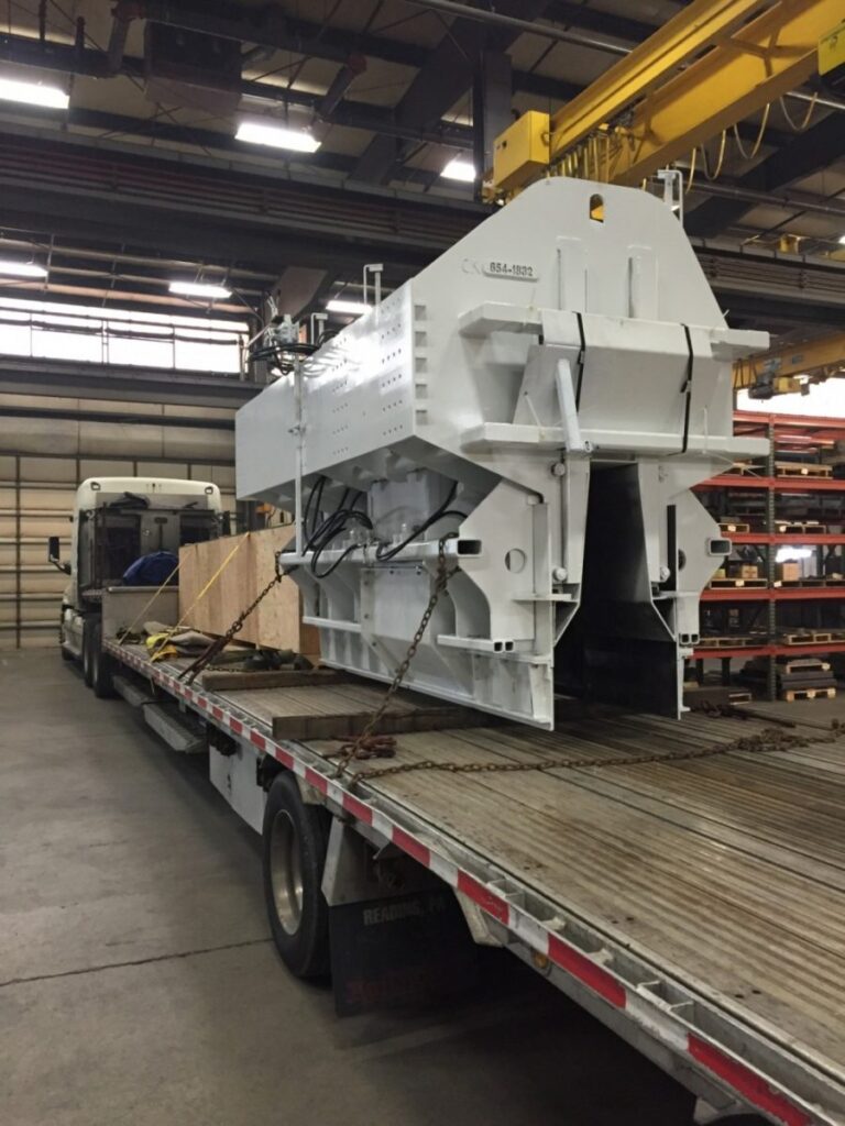 Miller Formless machine component crated and chained to a flatbed trailer inside a manufacturing warehouse.