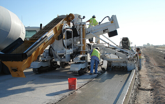 Miller Formless M-8800 multipurpose machine paving concrete with a conveyor feed and workers guiding the pour.