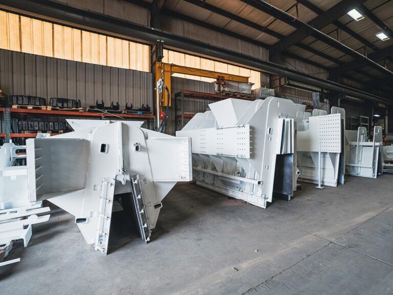 Assortment of white concrete mold attachments and machine parts staged on a warehouse floor near storage racks.