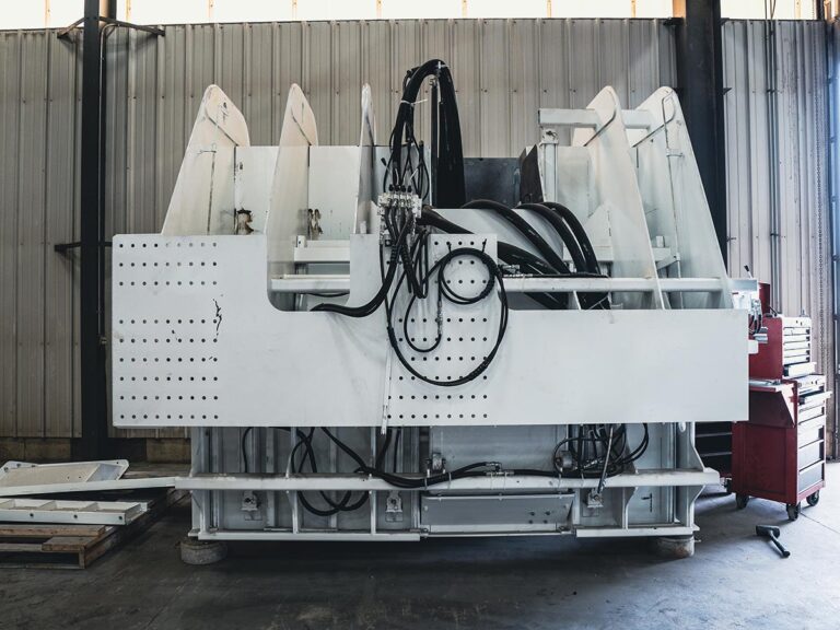 Back panel of a large white concrete mold assembly with hydraulic hoses and fittings in a warehouse.