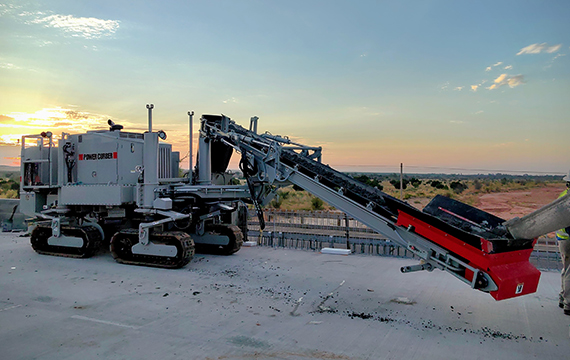 Power Curber 5704 machine with an auger attachment on a paved site at sunset.