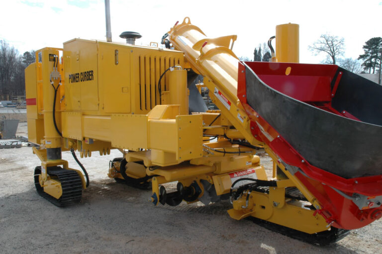 Yellow Power Curber machine with an auger and red hopper attachment parked on a gravel lot.