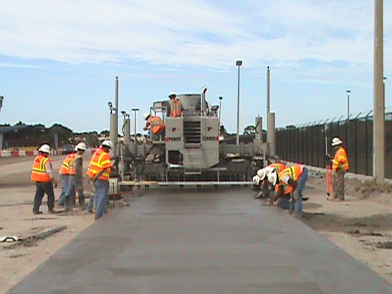 Power Curber machine placing an asphalt path as several workers in orange safety vests finish the surface.