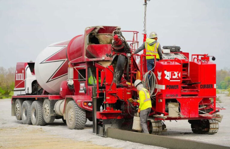 Power Curber 5700-D machine branded in red for PX placing concrete curb and gutter as a ready-mix truck feeds material and two workers guide the pour.