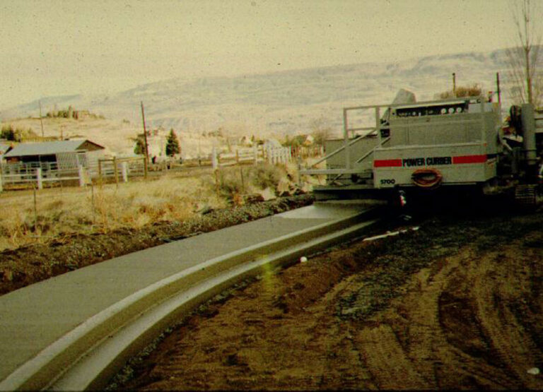 Archival photo of a Power Curber 5700 machine placing a monolithic curb and roadway with mountains in the background.