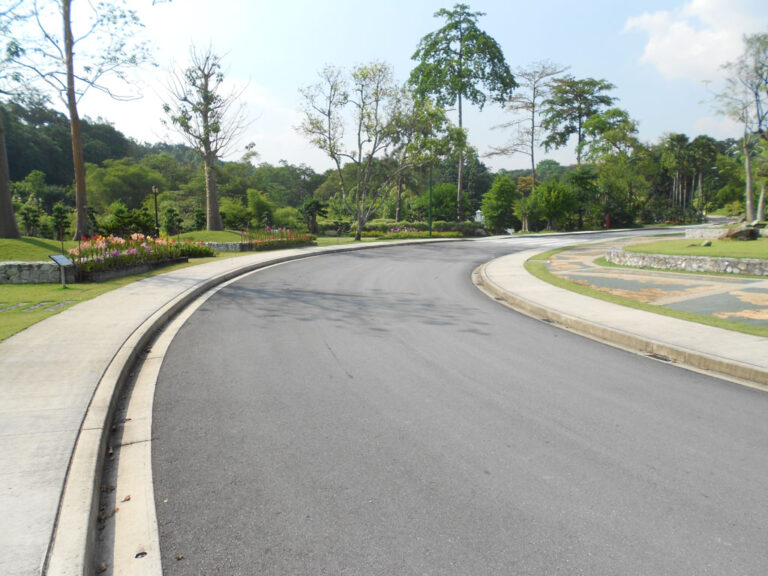 Curved monolithic concrete curb and sidewalk winding through a landscaped park with trees and flower beds.