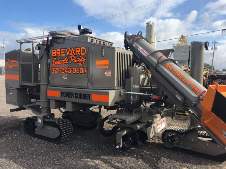 Power Curber machine branded for Brevard Concrete Paving in gray and orange, showing its conveyor arm and mold.