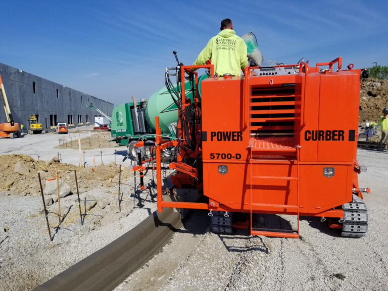 Orange Power Curber 5700-D machine branded for Campbell Concrete placing curb and gutter at a commercial construction site.
