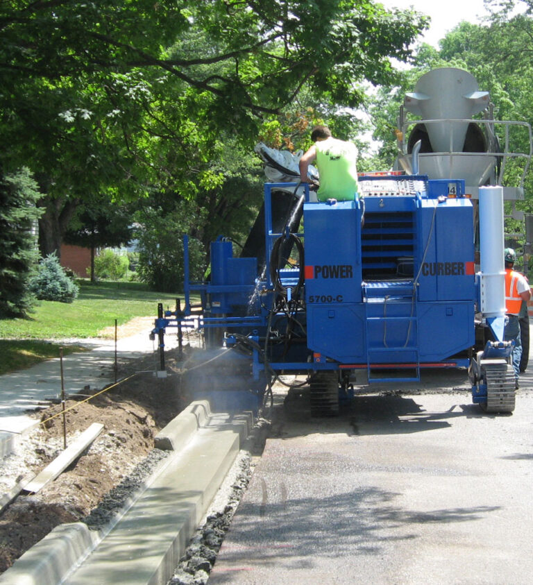 Blue Power Curber 5700-C machine placing a residential curb along a tree-lined street.