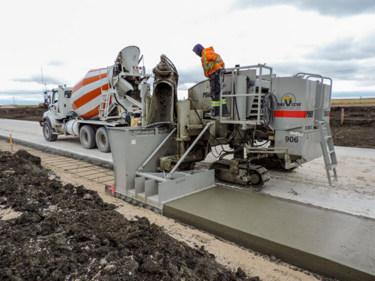 Power Curber 5700-C machine branded Bay View Construction placing a concrete sidewalk over rebar mesh with a ready-mix truck feeding material.