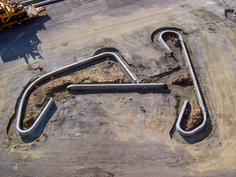 Aerial view of a zigzagging concrete barrier wall with tight-radius turns formed around a paved lot.