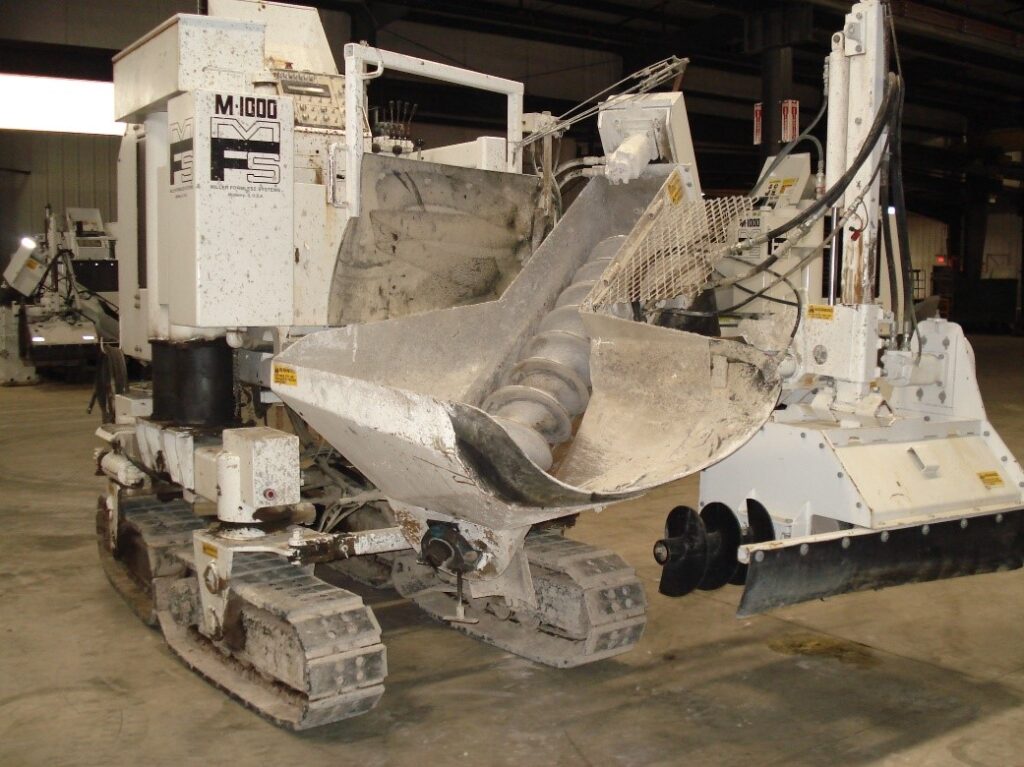 Miller Formless M-1000 machine parked in a warehouse, showing its worn auger conveyor and mold assembly.